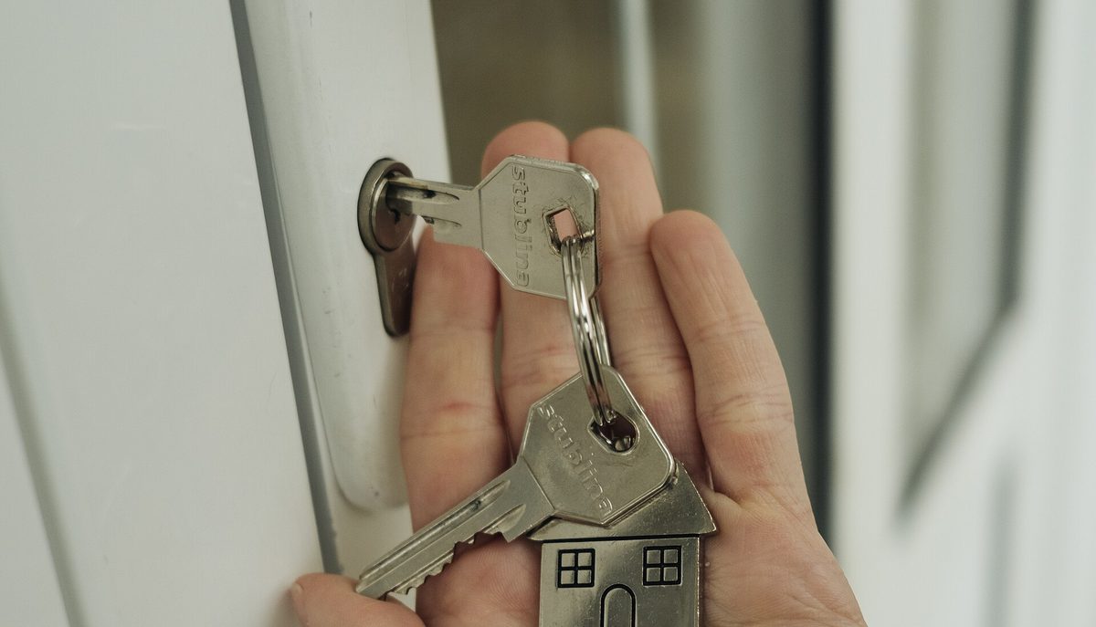 Mano con un llavero en forma de casa introduciendo las llaves en la puerta de una vivienda