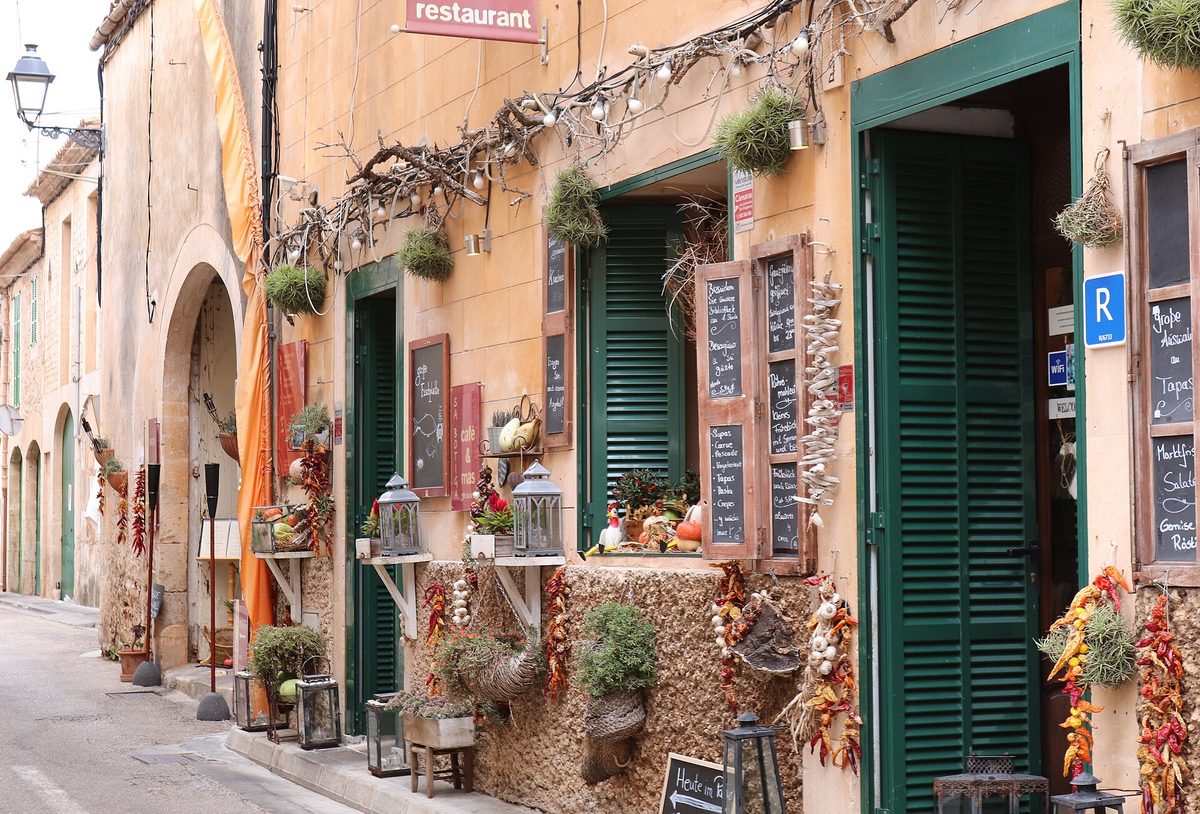 Calle con locales de restauración y comercios, con pizarras de menú y toldos, en Mallorca